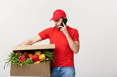 Kağıt kutusu gıda ile tutarak ve cep telefonu gri arka plan üzerinde izole ile arama yapma teslimatçı.