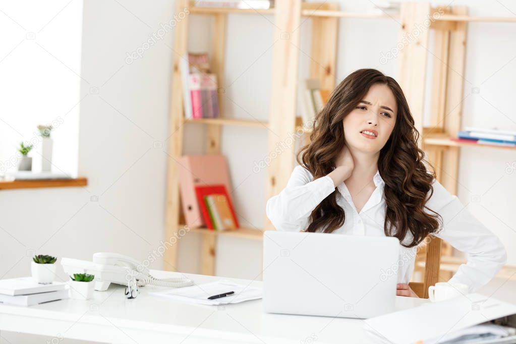 Tired young businesswoman suffering from long time sitting at computer desk in office