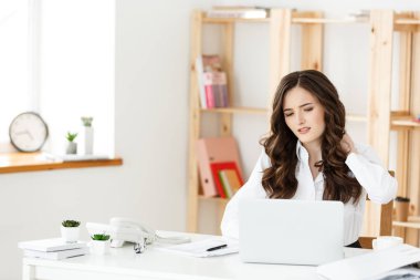 Uzun zamandır ofisteki bilgisayar masasında oturan yorgun genç iş kadını