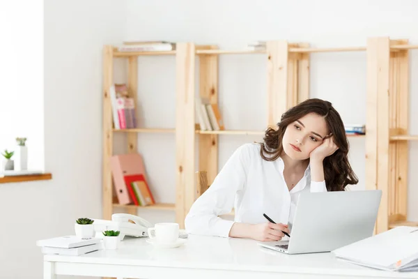 Trött vacker affärskvinna håller handen på huvudet medan du arbetar på datorn och vissa affärsdokument i ljusa kontor — Stockfoto