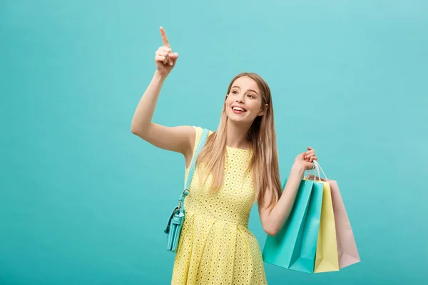 Shopping-Konzept: Porträt eines aufgeregten schönen Mädchens in gelbem Kleid mit Einkaufstaschen vor blauem Hintergrund — Stockfoto