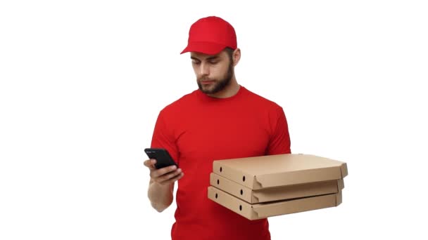 Szállítási fiú egy vörös egységes gazdaság egy halom pizza dobozok és ellenőrzése érdekében a mobiltelefon. Elszigetelt fehér háttér felett. — Stock videók