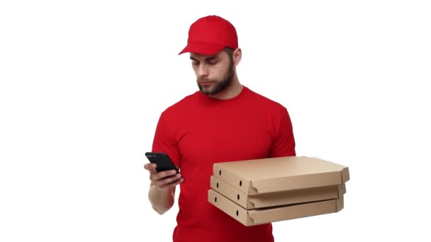 Repartidor con uniforme rojo sosteniendo una pila de cajas de pizza y comprobando la orden en el teléfono móvil. Aislado sobre fondo blanco . — Vídeos de Stock