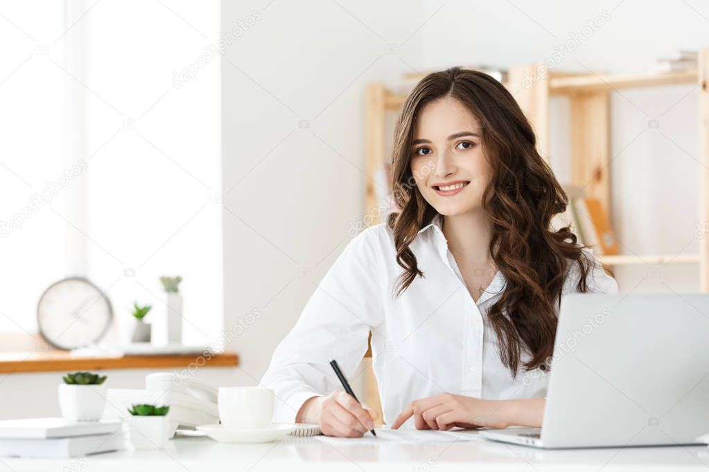 Smiling young woman making notes while sitting in the office.