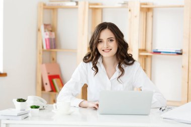 Gülümseyen genç kadın ofiste dizüstü bilgisayar önünde oturup.