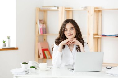 Gülümseyen genç kadın ofiste dizüstü bilgisayar önünde oturup.