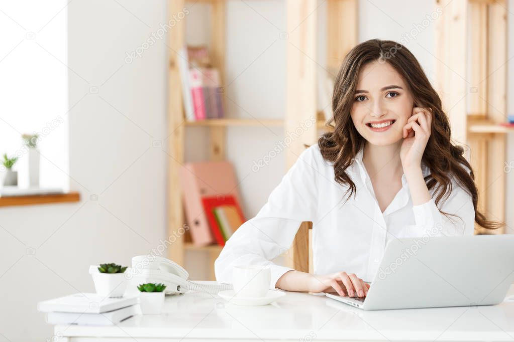Smiling young woman sitting in front of notebook in the office.