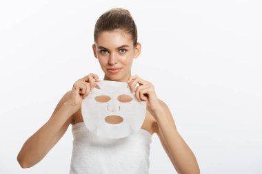 Yüzünde maske olan genç bir kız beyaz arka plandan kameraya bakıyor. Kozmetik prosedürü. Güzellik kaplıcası ve kozmetoloji.