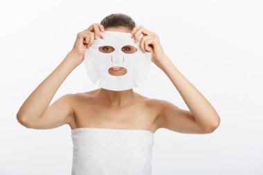 Yüzünde maske olan genç bir kız beyaz arka plandan kameraya bakıyor. Kozmetik prosedürü. Güzellik kaplıcası ve kozmetoloji