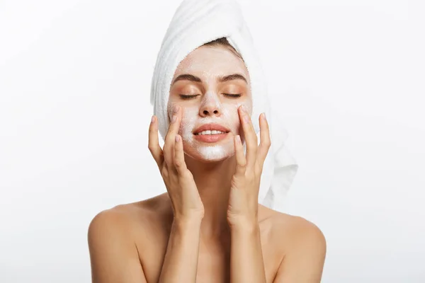Привлекательная молодая женщина, завернутая в банные полотенца, нанося крем на лицо после душа в ванной комнате . — стоковое фото