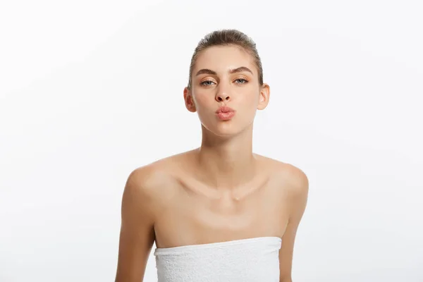 Довольно игривая молодая женщина в полотенце отправляет поцелуй на белом фоне — стоковое фото