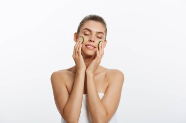 Mutlu bir güzel yarı çıplak kadın güzellik portresi kadar salatalık dilimleri, beyaz arka plan üzerinde izole yüzünü tutarak vücudu sarılı bir havlu ile kapatın