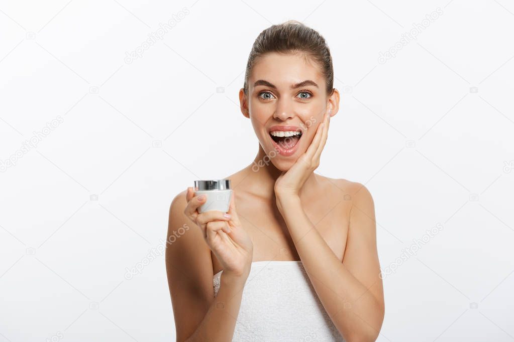 a surprised woman with a towel on her body applies a cream on the face skin.