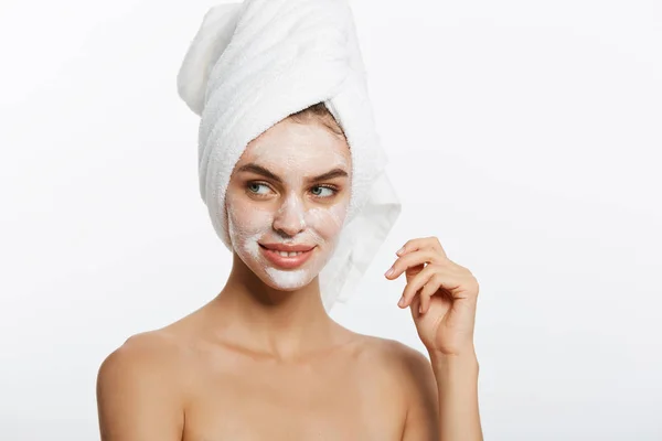 Mujer joven que aplica crema hidratante en su cara. Foto de mujer en albornoz blanco y toalla sobre fondo blanco. Concepto de cuidado de la piel —  Fotos de Stock