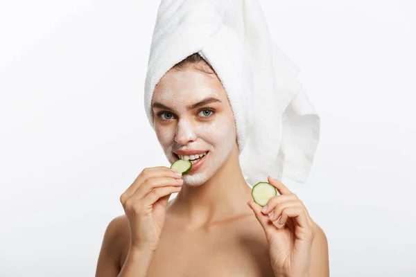 漂亮的年轻的自然女孩与完美的清洁皮肤看着相机吃黄瓜片在白色的背景。面部护理. — 图库照片