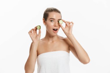 Genç güzel, mutlu kadın bazı salatalık gülümseyen yüzünü önünde tutuyor. Beyaz arka plan üzerinde izole.