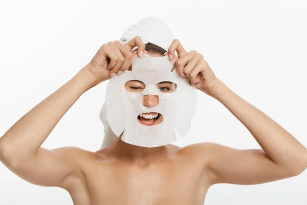 Ung flicka med ansiktsmask tittar på kameran över vit bakgrund. Kosmetisk procedur. Skönhet spa och kosmetologi. — Stockfoto