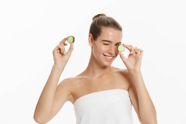 Genç güzel, mutlu kadın bazı salatalık gülümseyen yüzünü önünde tutuyor. Beyaz arka plan üzerinde izole.