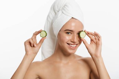 Bir gülümseyen güzel yarı çıplak kadın güzellik portresi kadar salatalık dilimleri tutarak ve beyaz arka plan üzerinde izole kamera bakarak saçlarını sarılı bir havlu ile kapatın