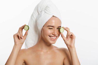 Bir gülümseyen güzel yarı çıplak kadın güzellik portresi kadar salatalık dilimleri tutarak ve beyaz arka plan üzerinde izole kamera bakarak saçlarını sarılı bir havlu ile kapatın