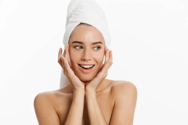 Έκπληκτος όμορφη νεαρή γυναίκα μετά το μπάνιο που αγγίζει το πρόσωπό της με μια πετσέτα στο κεφάλι της που απομονώνονται σε μπλε φόντο. Φροντίδα του δέρματος και το θέμα του Spa — Φωτογραφία Αρχείου