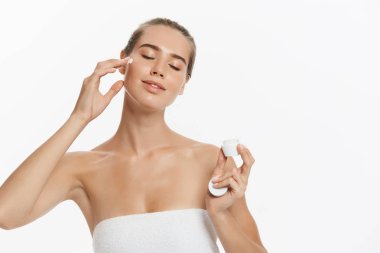 Yüzünde beyaz arka plan üzerinde izole kozmetik krem tedavisi uygulayarak güzel genç kadın