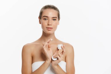 Yüzünde beyaz arka plan üzerinde izole kozmetik krem tedavisi uygulayarak güzel genç kadın