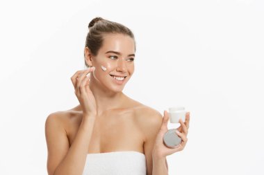 Yüzünde beyaz arka plan üzerinde izole kozmetik krem tedavisi uygulayarak güzel genç kadın