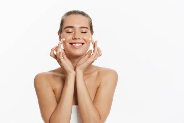 Yüzünde beyaz arka plan üzerinde izole kozmetik krem tedavisi uygulayarak güzel genç kadın