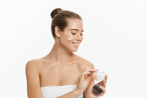 Mulher bonita aplicando tratamento de creme cosmético em seu rosto isolado no fundo branco — Fotografia de Stock