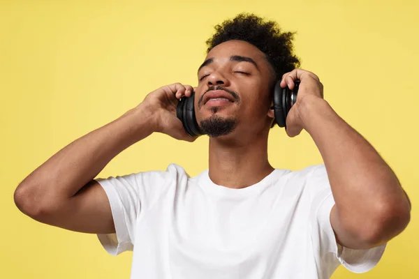 Attraktiver afrikanisch-amerikanischer Mann mit Kopfhörern hört Musik. isoliert über gelbem Gold Hintergrund. — Stockfoto