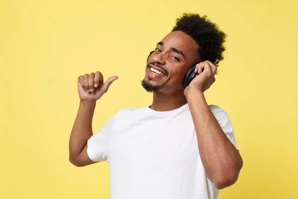 Attraktiver afrikanisch-amerikanischer Mann mit Kopfhörern hört Musik. isoliert über gelbem Gold Hintergrund. — Stockfoto