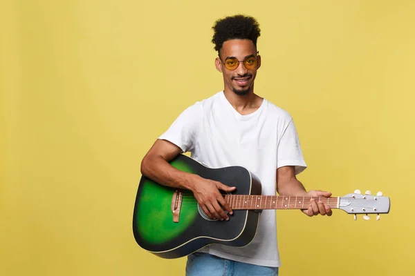 Glücklicher afrikanisch-amerikanischer Musiker, der mit einer Gitarre vor goldgelbem Hintergrund posiert. — Stockfoto