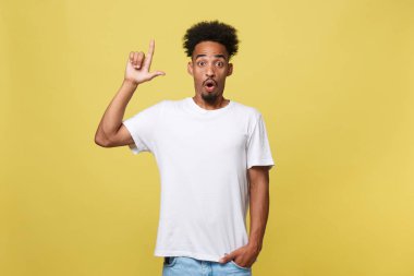 İşaret parmağı kopya alanı metin veya promosyon içeriği için altın sarı zemin üzerine, bak, şaşırmış gibi genç giyinmiş Afrikalı-Amerikalı adam heyecanlı rahat beyaz gömleği giyince hayran