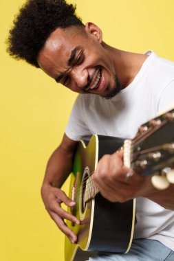 Genç yakışıklı Afro-Amerikan retro gitarist izole sarı altın arka plan üzerinde akustik gitar çalmak tarz.