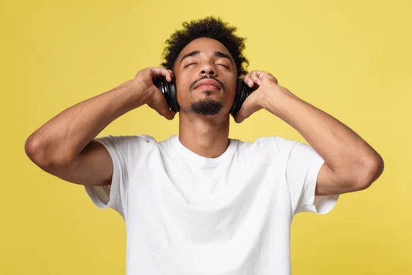 Junger afrikanisch-amerikanischer Mann trägt Kopfhörer und genießt Musik über gelbgoldenem Hintergrund — Stockfoto