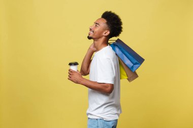 Alışveriş çantası ve take away kahve fincanı ile yakışıklı Afrikalı-Amerikalı. Sarı altın arka plan üzerinde izole.