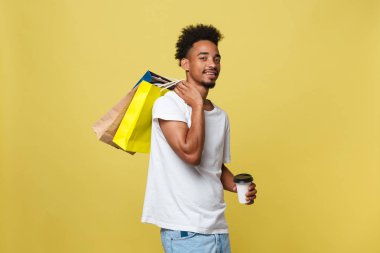 Alışveriş çantası ve take away kahve fincanı ile yakışıklı Afrikalı-Amerikalı. Sarı altın arka plan üzerinde izole.