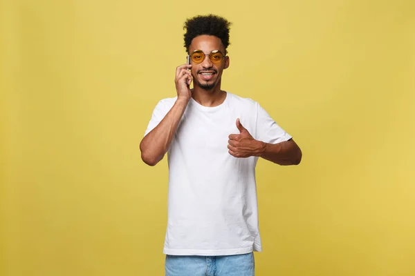 Portrait of cool young black guy talking on cellphone. Isolated on yellow background — Stock Photo, Image