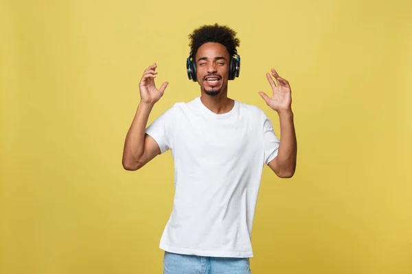 Joven hombre afroamericano con auriculares y disfrutar de la música sobre oro amarillo Fondo —  Fotos de Stock