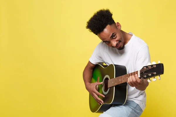 Jovem bonito Africano americano retro estilo guitarrista tocando guitarra acústica isolada no fundo de ouro amarelo . — Fotografia de Stock