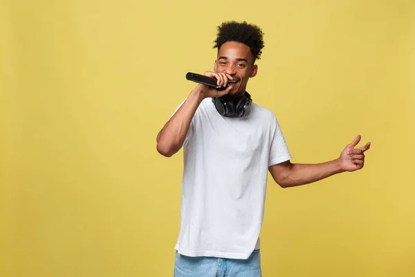 Mladý pohledný African American mužské zpěvák provedení s mikrofonem. Samostatný žlutý zlaté pozadí. — Stock fotografie