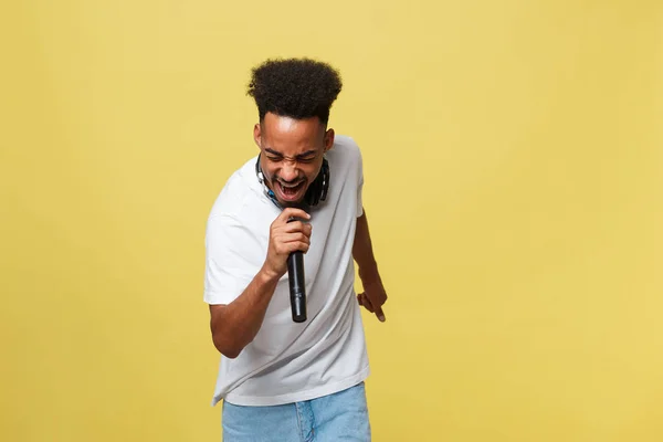 Junger, gut aussehender afrikanisch-amerikanischer Sänger, der mit Mikrofon auftritt. isoliert über gelbem Gold Hintergrund. — Stockfoto