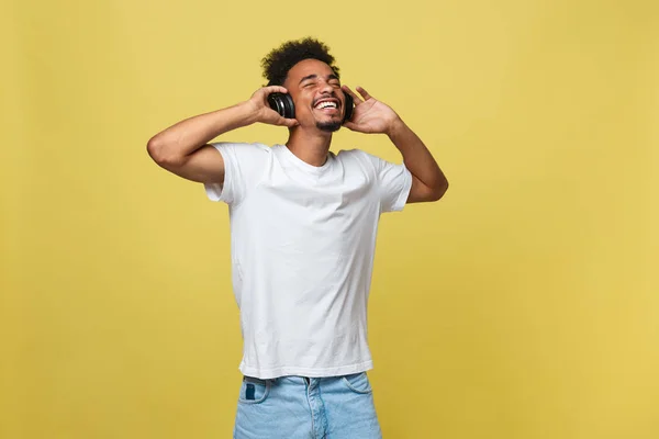 Junger schwarzer Mann, der über Kopfhörer Musik hört. isoliert über gelbem Hintergrund. — Stockfoto