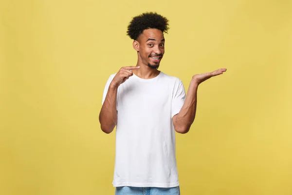 Charming handsome young black man holding his hand up to show present sell product. Isolated over yellow background. — Stock Photo, Image