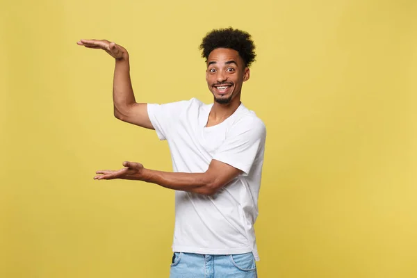 매력적인 잘생긴 젊은 흑인 남자 쇼 현재 판매 제품까지 그의 손을 잡고. 노란색 배경 위에 절연. — 스톡 사진