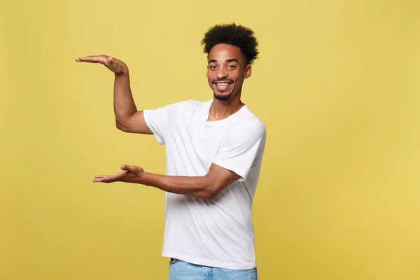 Okouzlující pohledný mladý černoch přidržoval ruku Ukázat současné prodat produkt. Na žlutém pozadí, samostatný. — Stock fotografie