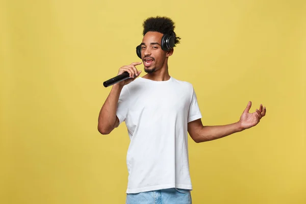 Aantrekkelijke jonge donkere man met afro kapsel in witte t shirt, gebaren met de handen en microfoon, dansen en zingen op partij, plezier. — Stockfoto