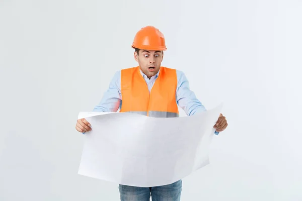 Shocked builder construction worker is holding in hand a plan draft document isolated on gray background. — Stock Photo, Image