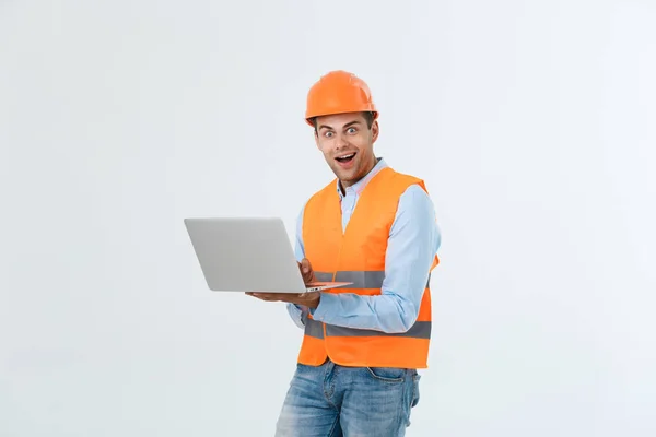 Adult man constructor surprised and working with laptop in helmet indoors. — Stock Photo, Image